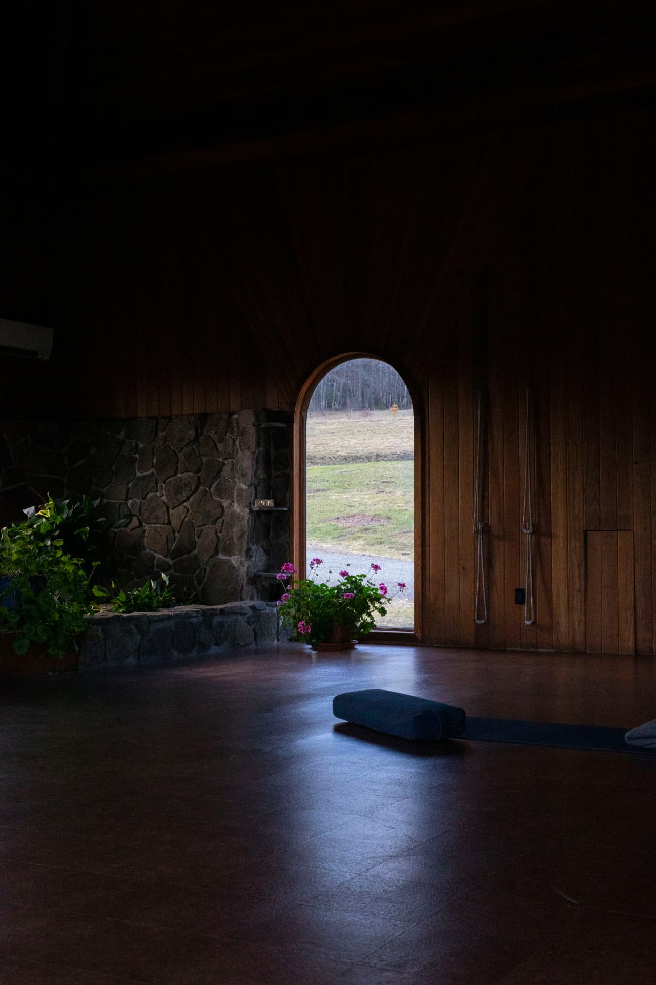 A quiet studio interior with stone walls, wooden floors, an arched doorway opening to a grassy field, and a yoga mat on the floor — the Soul Therapy practice space