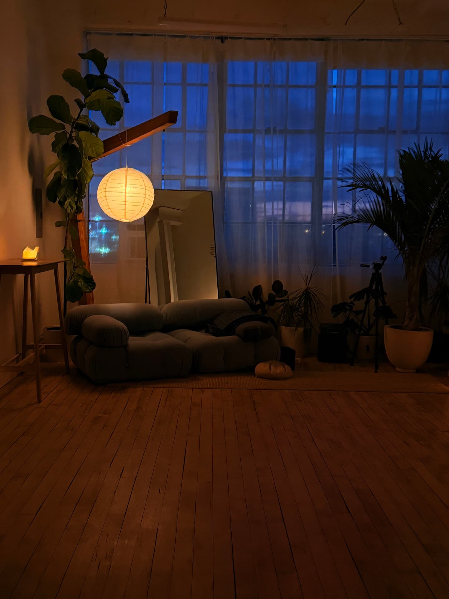 A soft sofa, plants, and a paper lantern glowing in the studio's window corner