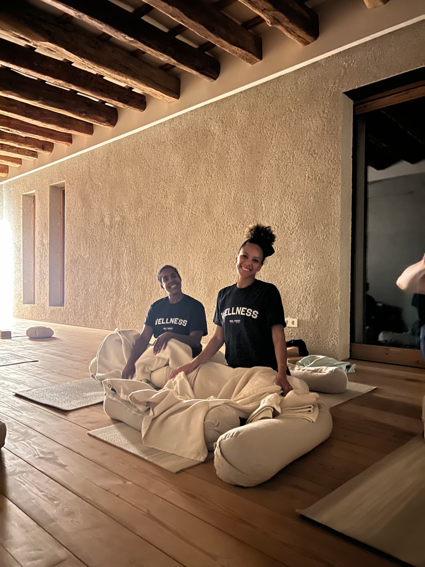 Two Soul Therapy teachers laying out bolsters and blankets in a beamed practice room