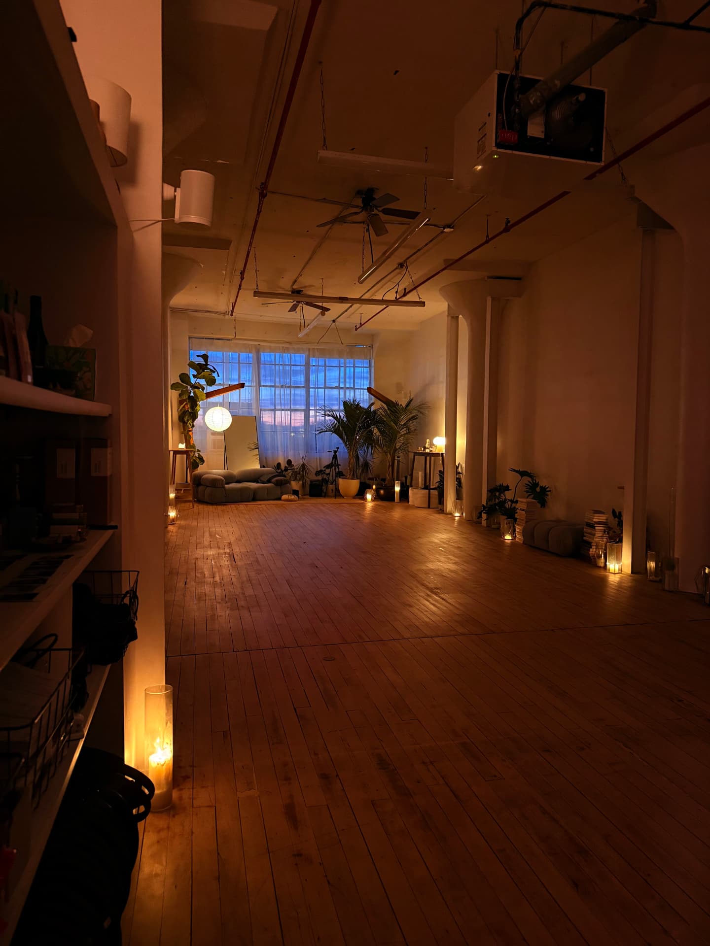 The studio at dusk, candles lining the wood floor and blue light in the windows